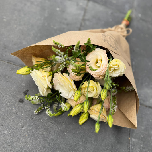 Bouquet of lisianthus flowers wrapped in brown paper on gray pavement